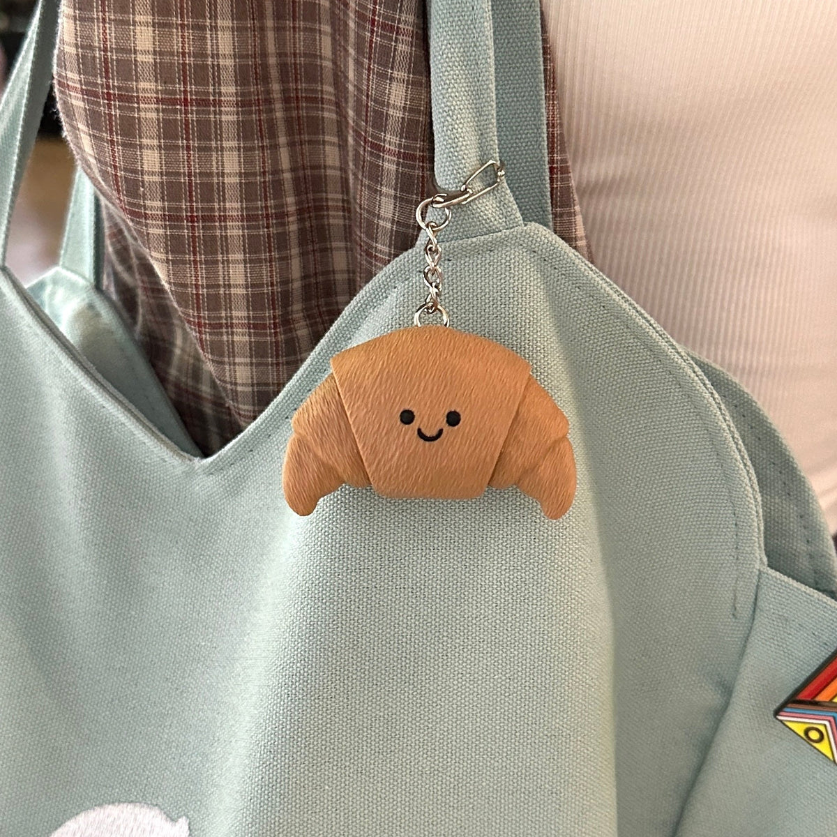 A croissant clicker keychain on a light blue-green fabric tote bag