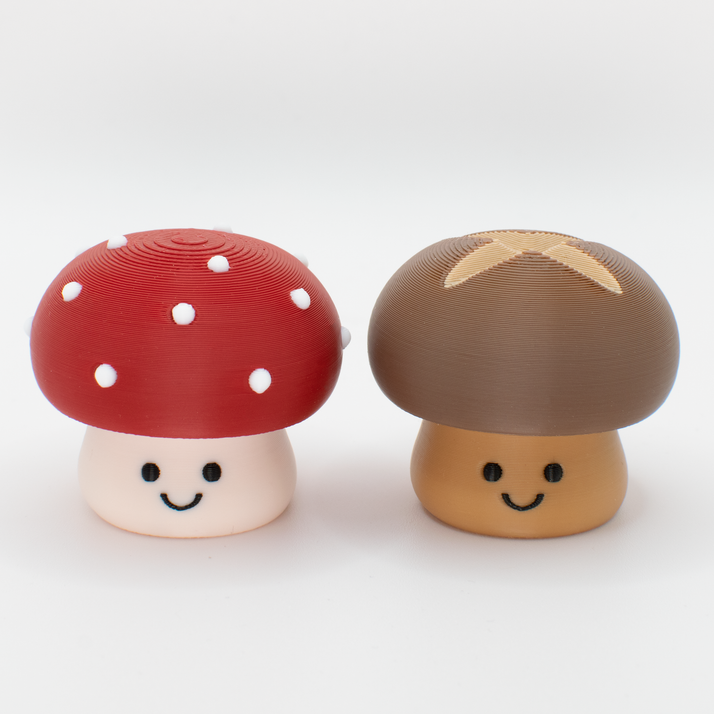 Two mushroom-shaped fidget toy desk decor, one red with white spots and one brown with a cross, both with a smiley face, on a white background.