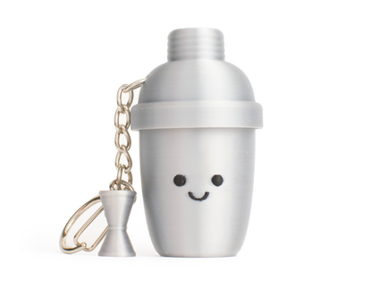 A silver-aluminum-color cocktail shaker fidget clicker keychain with a cute smiling face and a small matching hourglass-shaped measuring cup charm, set against a plain white background.