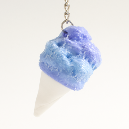 A cotton candy shaped fidget clicker, featuring a textured blue and purple swirled top and a white cone base, suspended from a silver metal chain against a plain white background.