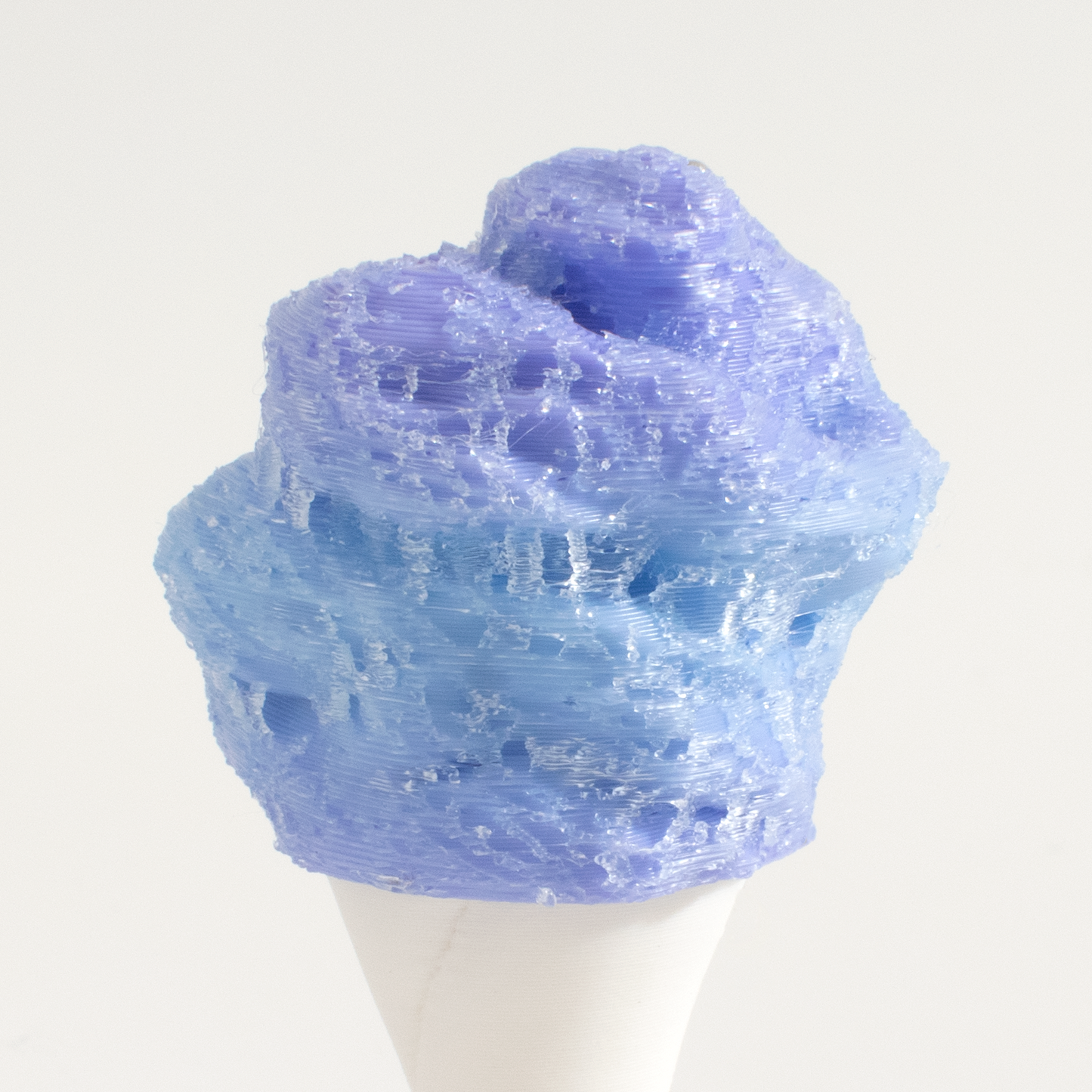 A 3D-printed, textured cotton candy fidget clicker filled with light blue and lavender-colored material, displayed on a white cone stand against a plain off-white background.