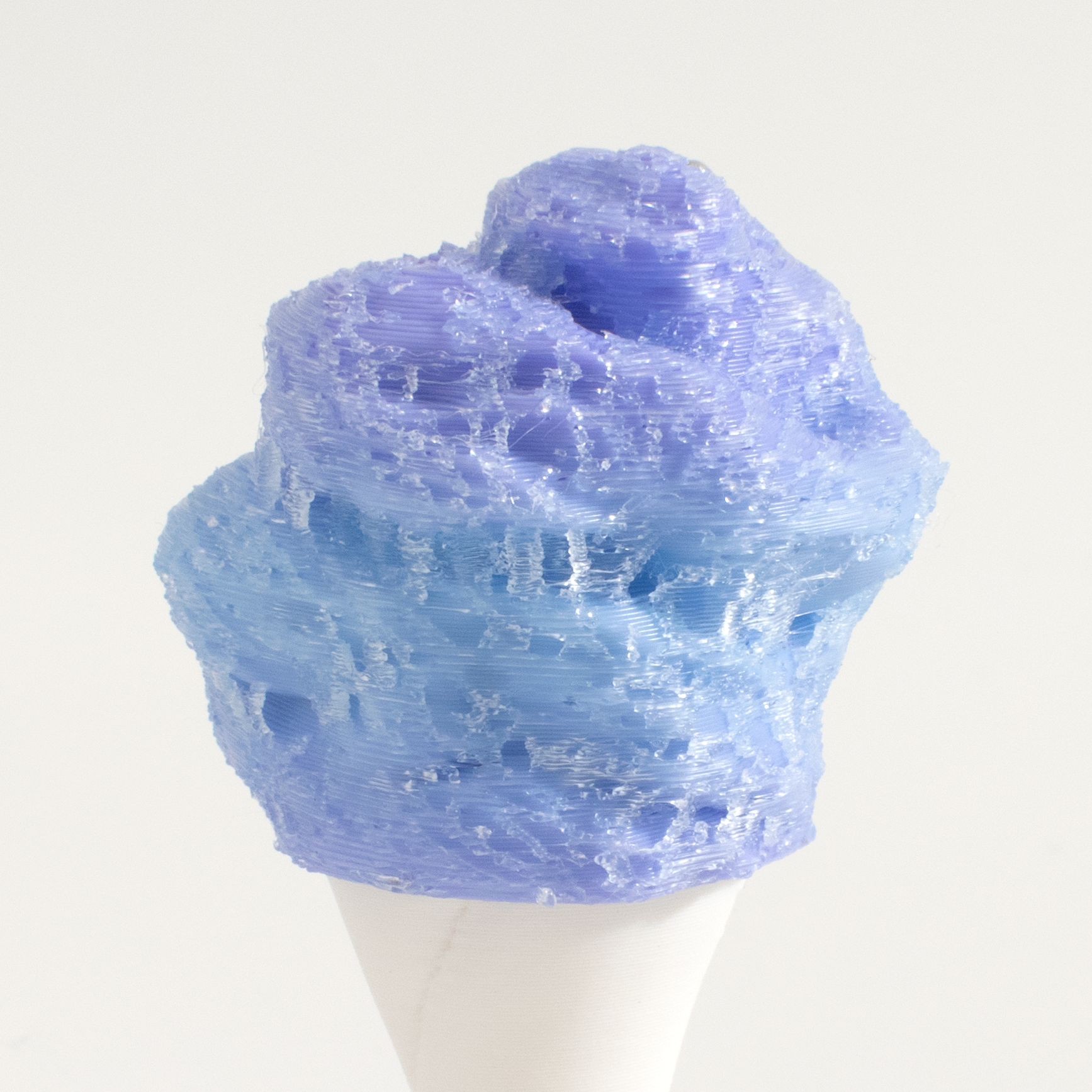 A 3D-printed, textured cotton candy fidget clicker filled with light blue and lavender-colored material, displayed on a white cone stand against a plain off-white background.
