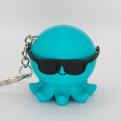 Turquoise octopus fidget clicker keychain with black sunglasses on a light gray background