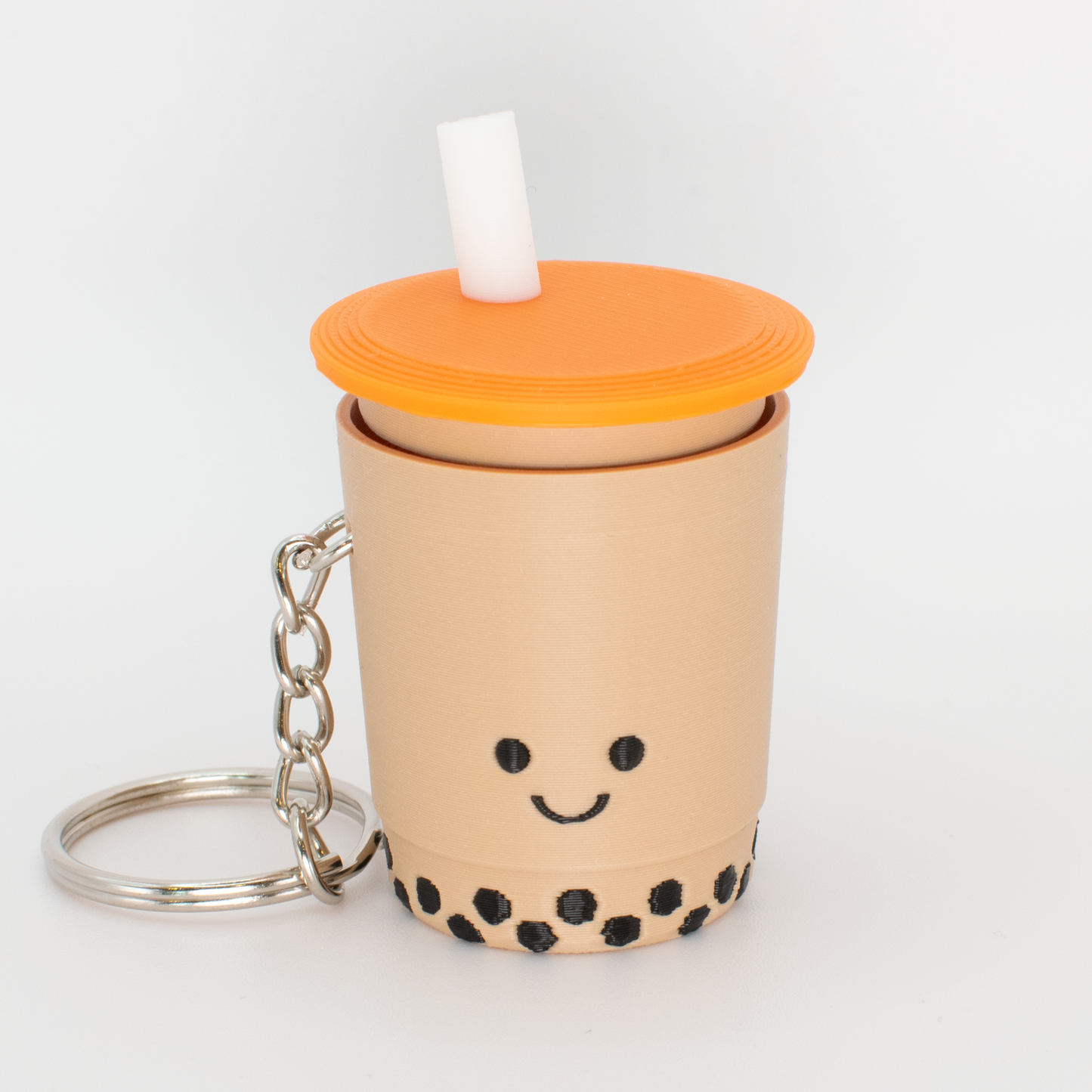 A fidget clicker resembling a cup of bubble tea with a smiling face, an orange lid, and a straw, attached to a keychain.