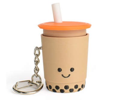 A fidget clicker resembling a cup of bubble tea with a smiling face, an orange lid, and a straw, attached to a keychain.