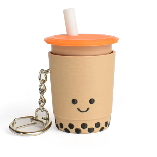 A fidget clicker resembling a cup of bubble tea with a smiling face, an orange lid, and a straw, attached to a keychain.