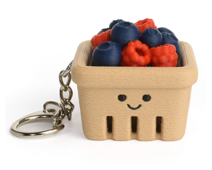 A small beige berry basket keychain with a smiling face, filled with faux blueberries and raspberries, attached to a silver metal key ring on a white background.