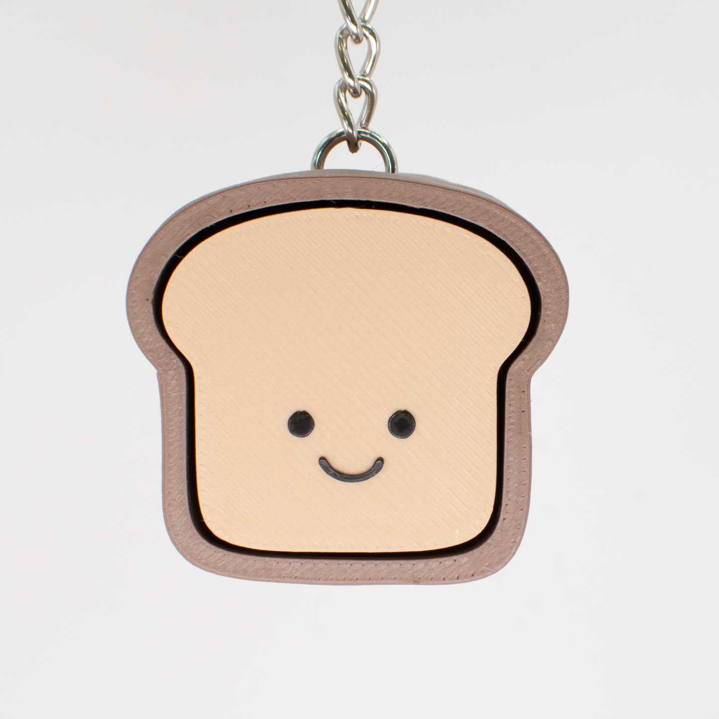 A fidget clicker toy designed to look like a smiling loaf of bread with a beige and brown color scheme, hung on a keychain that could serve as a bag charm