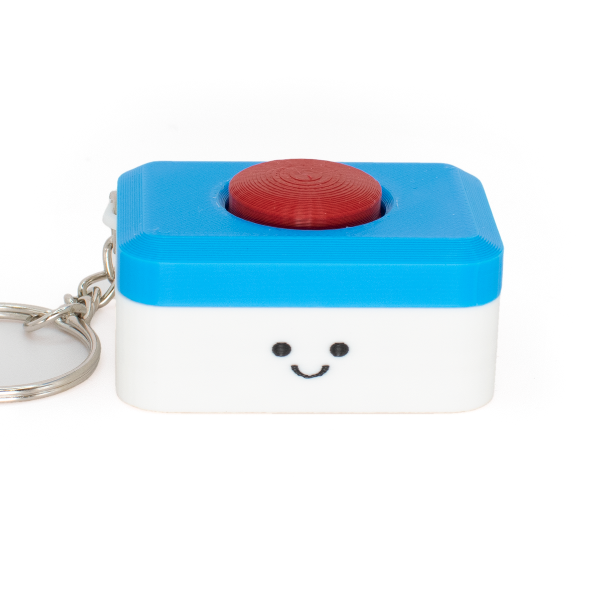 A small clicker keychain styled as a dishwasher tab with a smiling face on a white lower half and a bright blue top half, featuring a red circular button on top and a silver metal keyring, photographed on a white background.