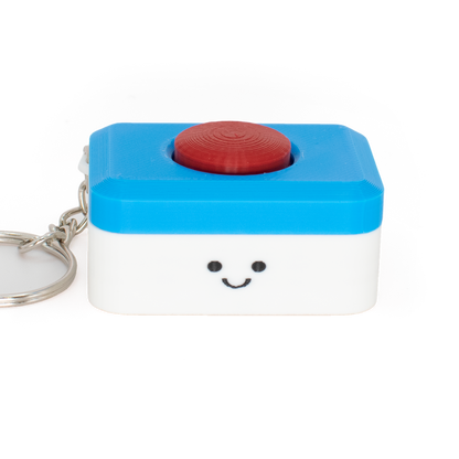 A small clicker keychain styled as a dishwasher tab with a smiling face on a white lower half and a bright blue top half, featuring a red circular button on top and a silver metal keyring, photographed on a white background.