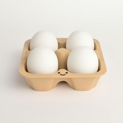 fidget clicker styled as four white eggs arranged in a light brown cardboard egg carton with a small smiley face printed on the front, set against a clean white background.