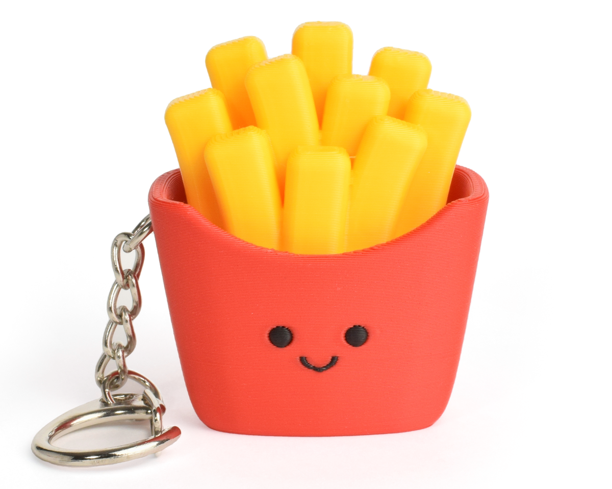 A small novelty keychain shaped like a basket of French fries. The basket is bright red with a simple black face, filled with yellow fries, and attached to a silver metal key ring on a plain white background.