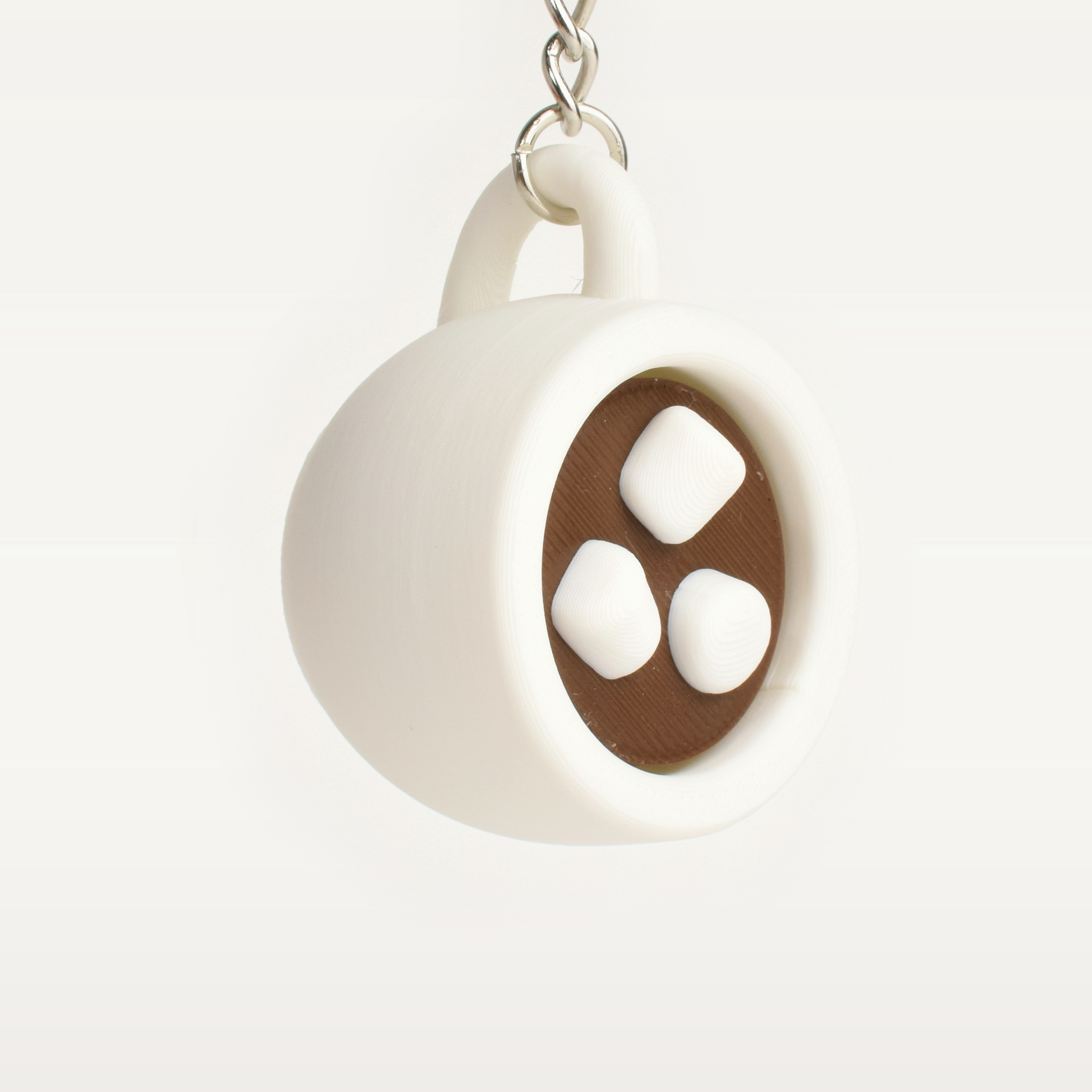 A novelty hot chocolate clicker keychain shaped like a cup with a brown interior and three marshmallows, suspended by a silver metal chain against a light gray gradient background.