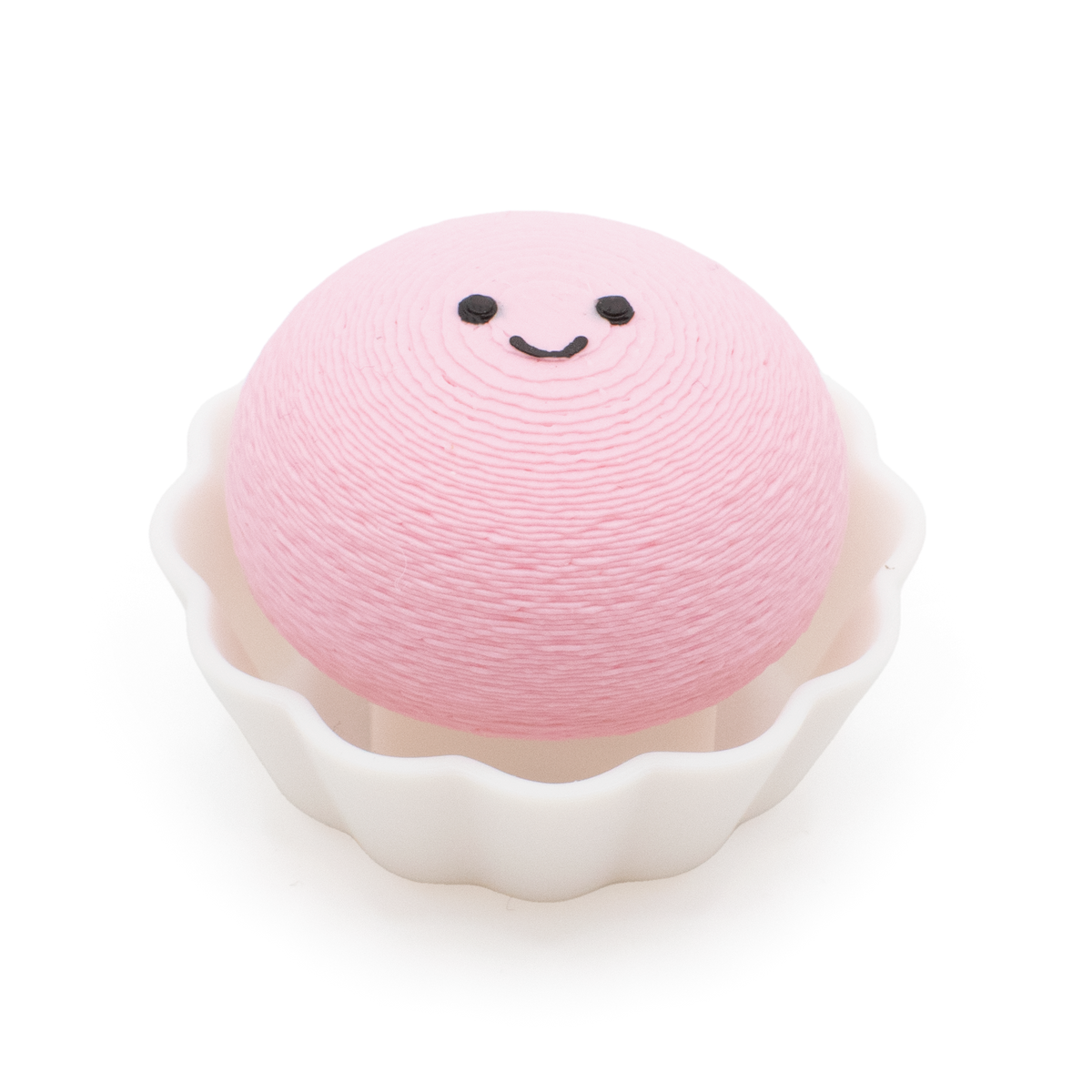 A pink, round mochi clicker with a simple smiley face sits inside a white cup on a plain white background.