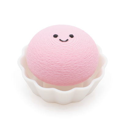 A pink, round mochi clicker with a simple smiley face sits inside a white cup on a plain white background.