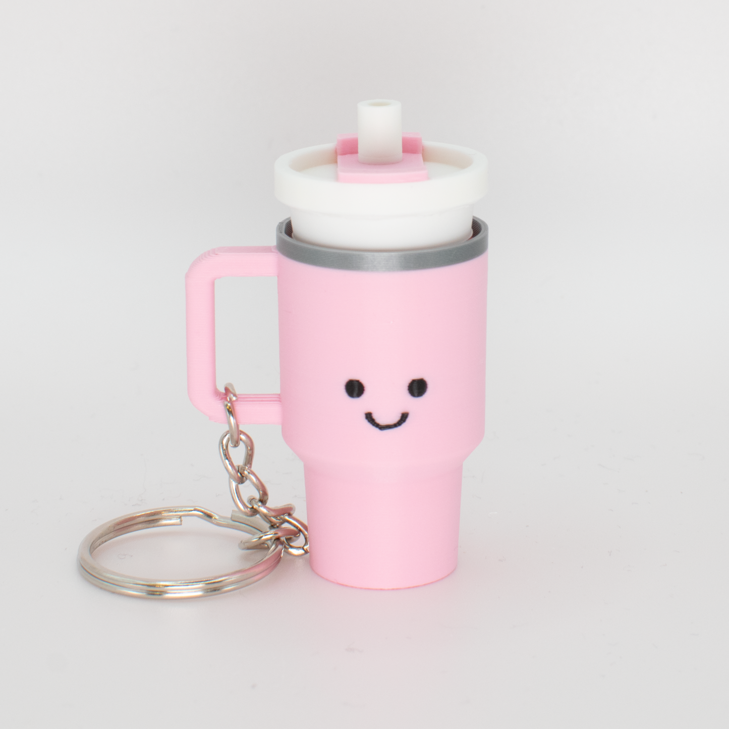 A pink tumbler fidget clicker with a smiling face and a clicky lid, attached to a keychain.