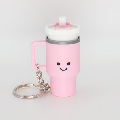 A pink tumbler fidget clicker with a smiling face and a clicky lid, attached to a keychain.