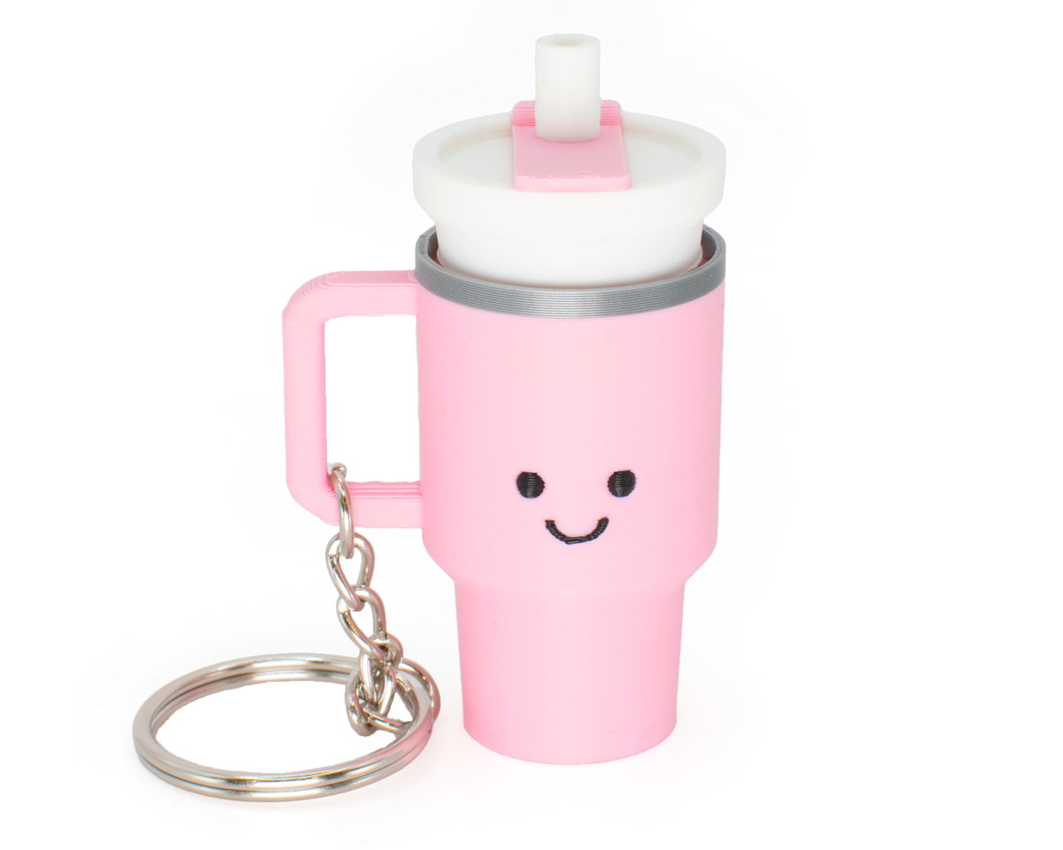 A pink tumbler fidget clicker with a smiling face and a clicky lid, attached to a keychain.