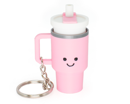 A pink tumbler fidget clicker with a smiling face and a clicky lid, attached to a keychain.