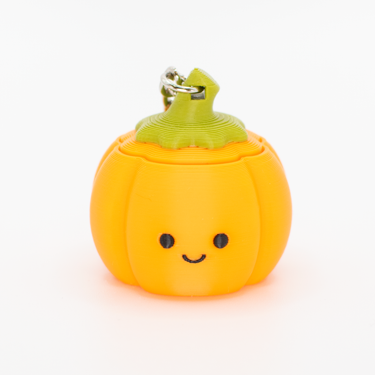 A cute orange pumpkin-shaped clicky stress toy with a green stem and a metal keyring, featuring a simple black smiley face, set against a plain white background.