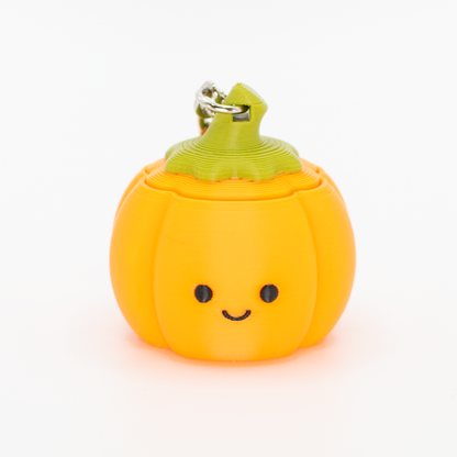 A cute orange pumpkin-shaped clicky stress toy with a green stem and a metal keyring, featuring a simple black smiley face, set against a plain white background.