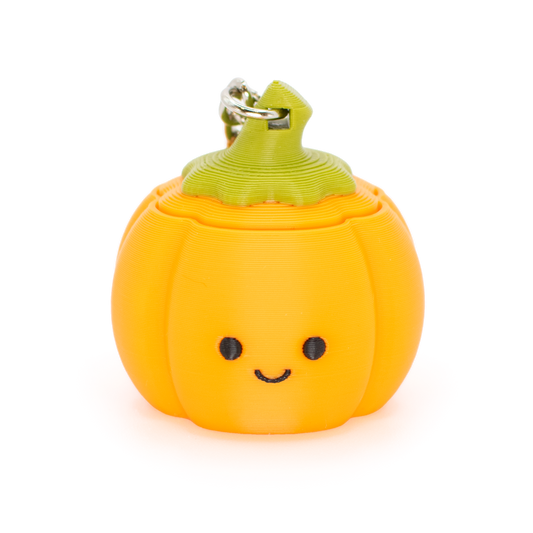 A cute orange pumpkin-shaped clicky stress toy with a green stem and a metal keyring, featuring a simple black smiley face, set against a plain white background.