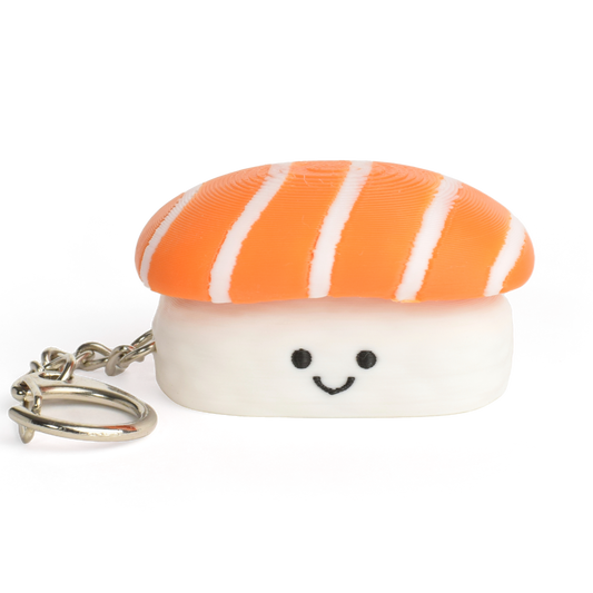 A small sushi-shaped clicker keychain with a smiling face, featuring a salmon top and a white rice base, attached to a silver metal key ring on a plain white background.