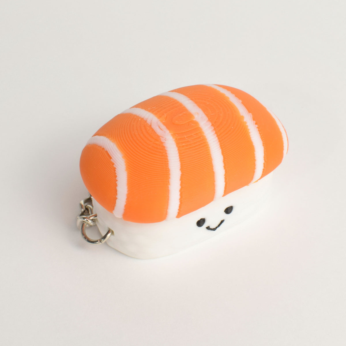 A small sushi-shaped clicker keychain with a slice of salmon top, white rice base, photographed on a plain white background.