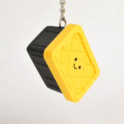 A small novelty keychain shaped like a tote bin, with a simple smiley face, suspended from a silver metal chain against a light gray background.