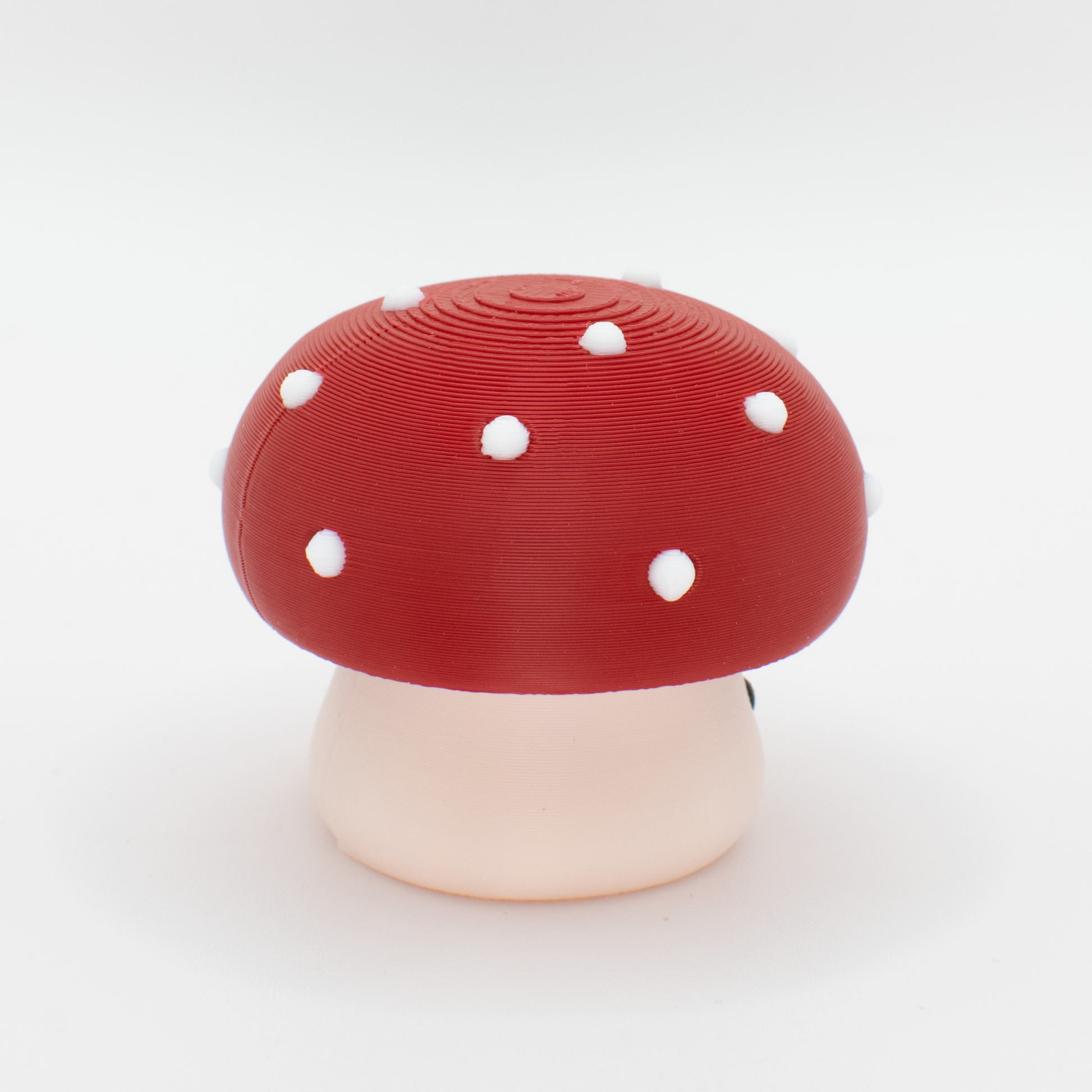 side view of a mushroom-shaped clicker with a red cap and white stem on a white background