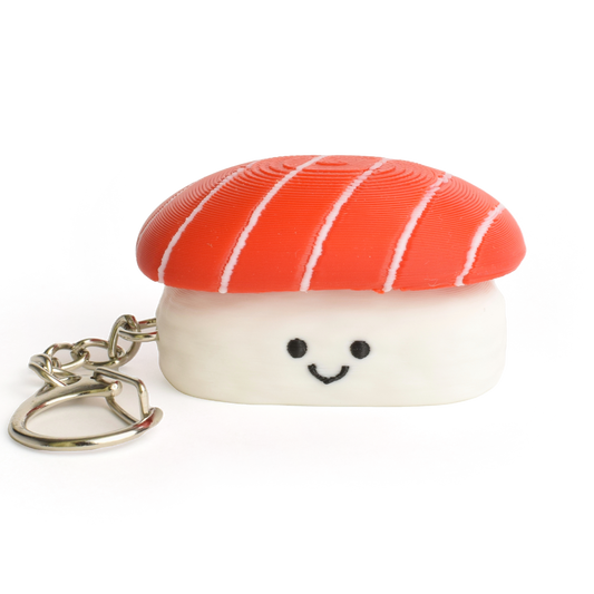 A small sushi-shaped clicker keychain with a smiling face, featuring a tuna top and a white rice base, attached to a silver metal key ring on a plain white background.