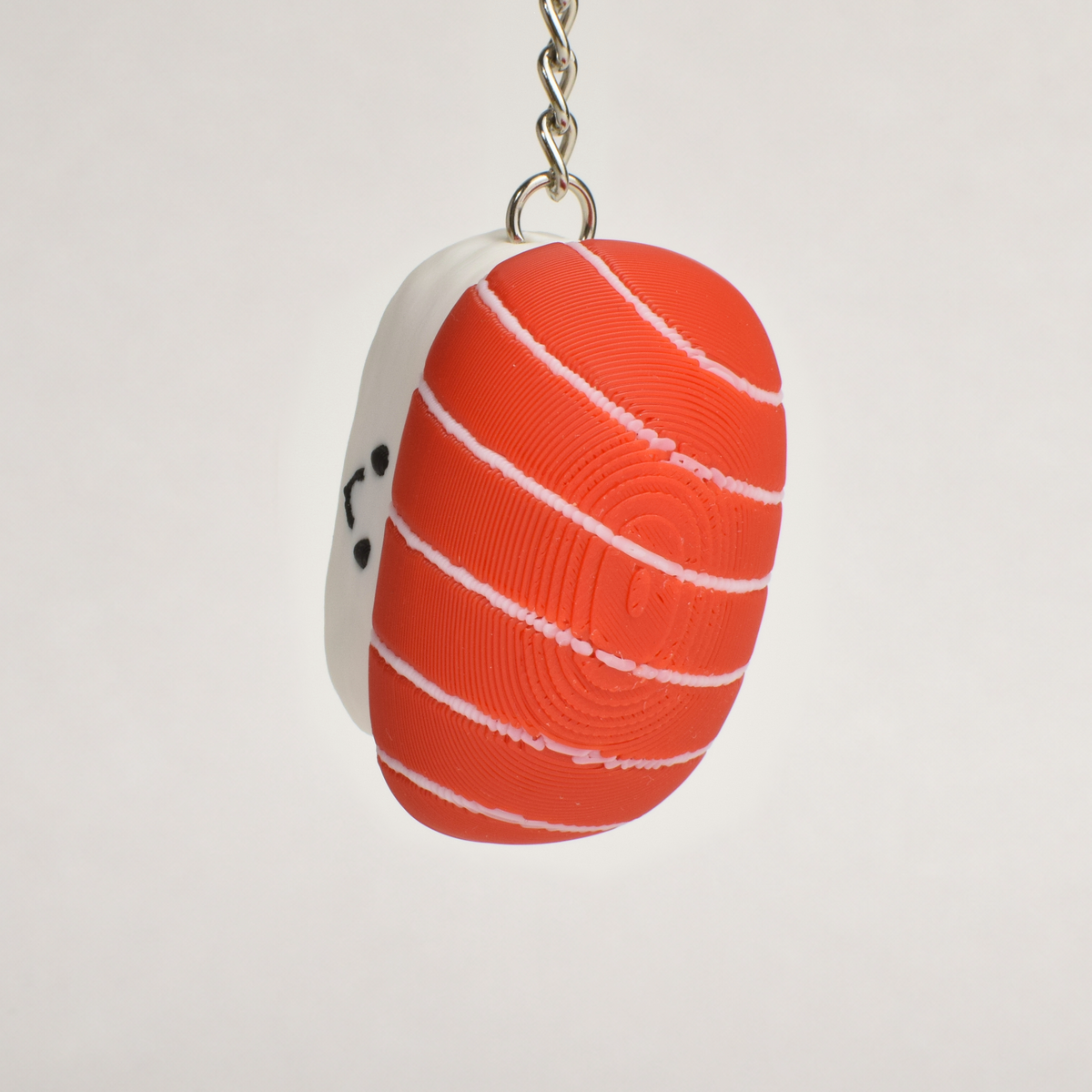 A small sushi-shaped clicker keychain with a smiling face, featuring a tuna top and a white rice base, attached to a silver metal key ring on a plain white background.