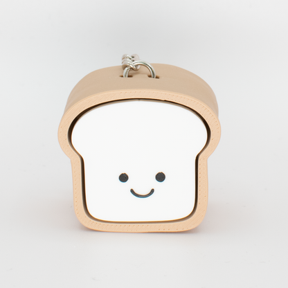 A toy clicker designed to look like a loaf of bread with a smiling face, primarily in beige and white colors.