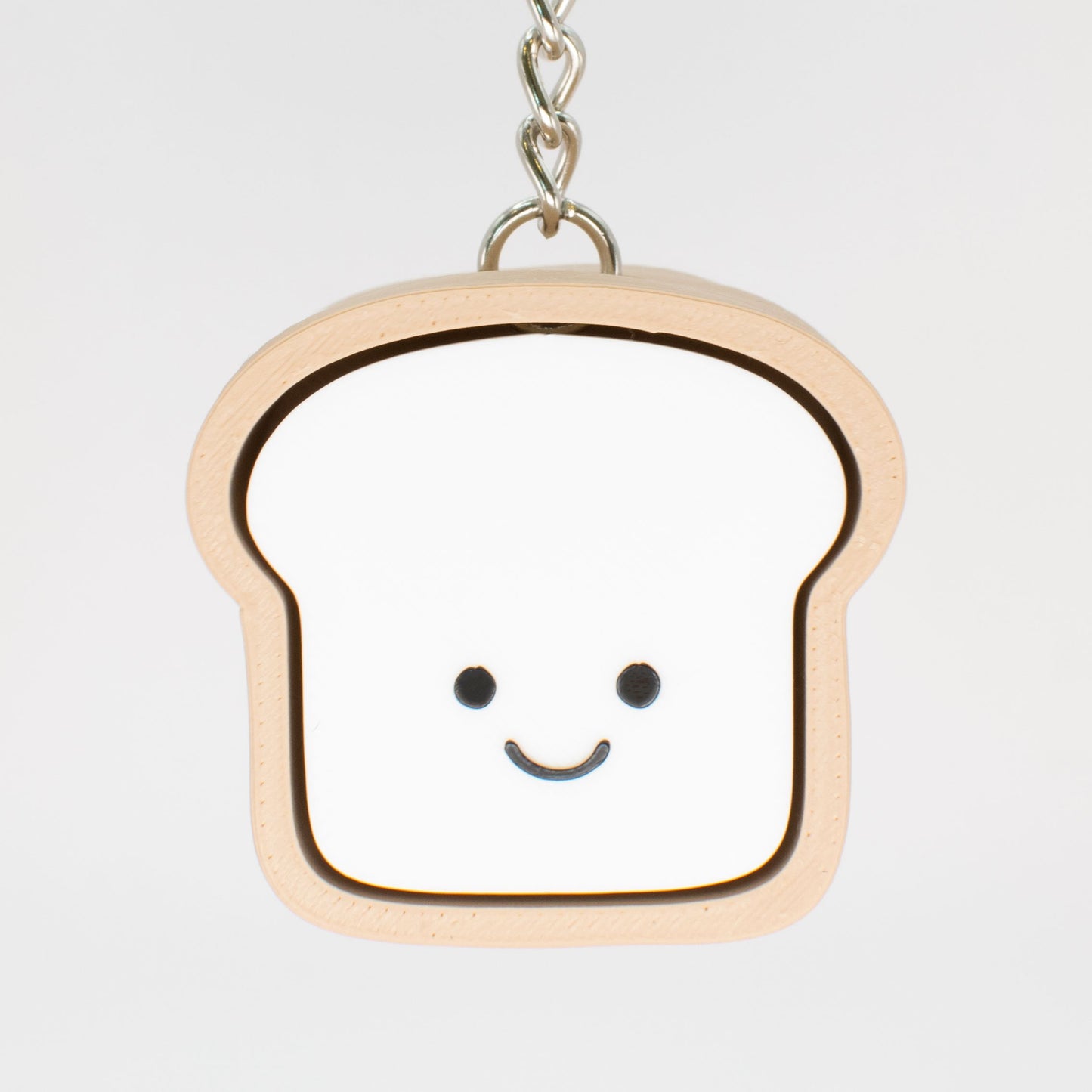 A fidget clicker toy designed to look like a smiling loaf of bread with a beige and white color scheme, hung on a keychain that could serve as a cute bag charm
