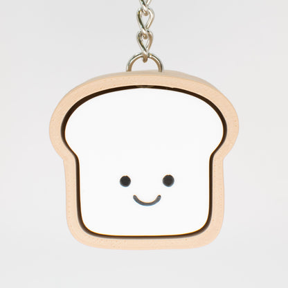 A fidget clicker toy designed to look like a smiling loaf of bread with a beige and white color scheme, hung on a keychain that could serve as a cute bag charm